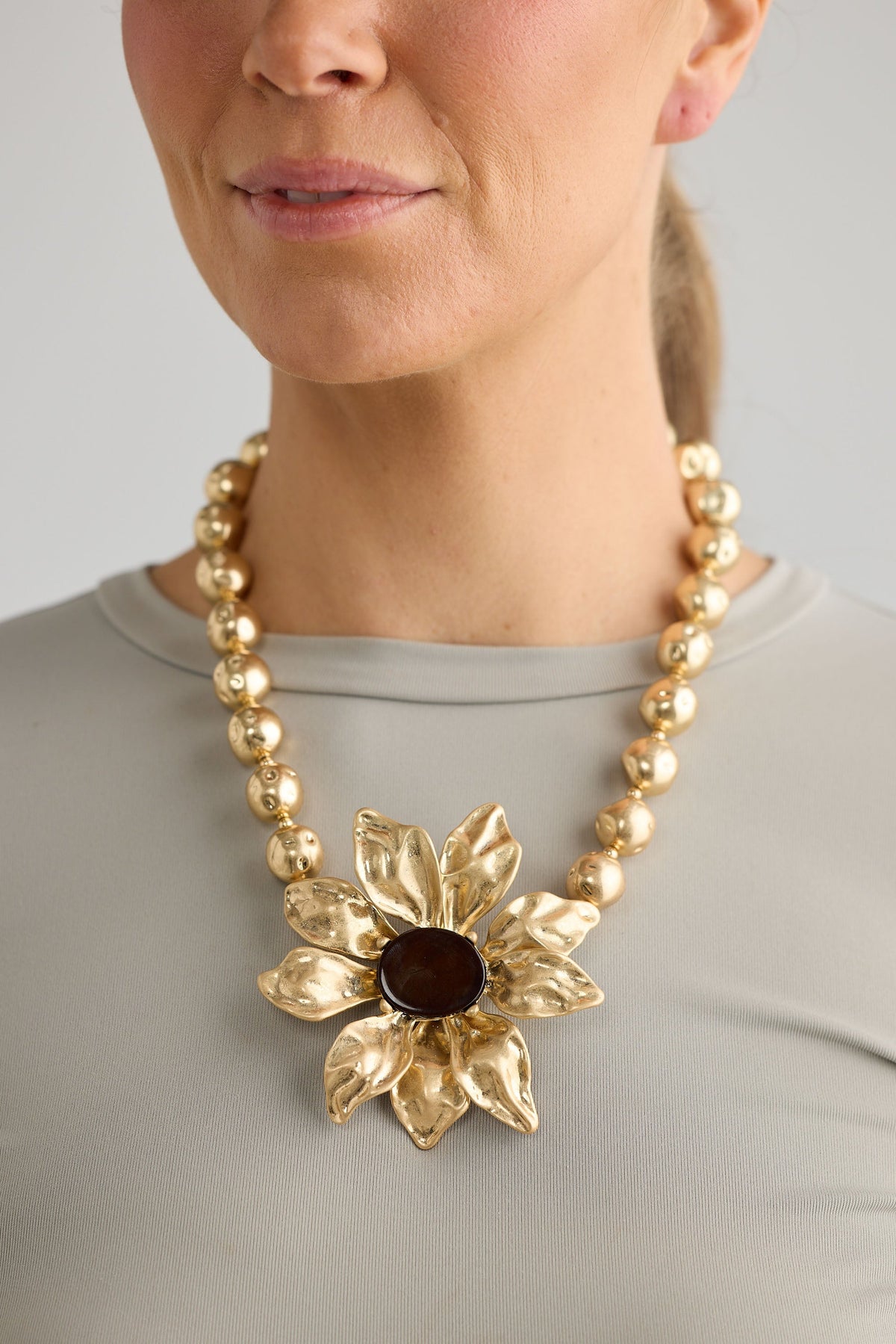 Gold necklace with a large floral pendant worn by a person against a neutral background