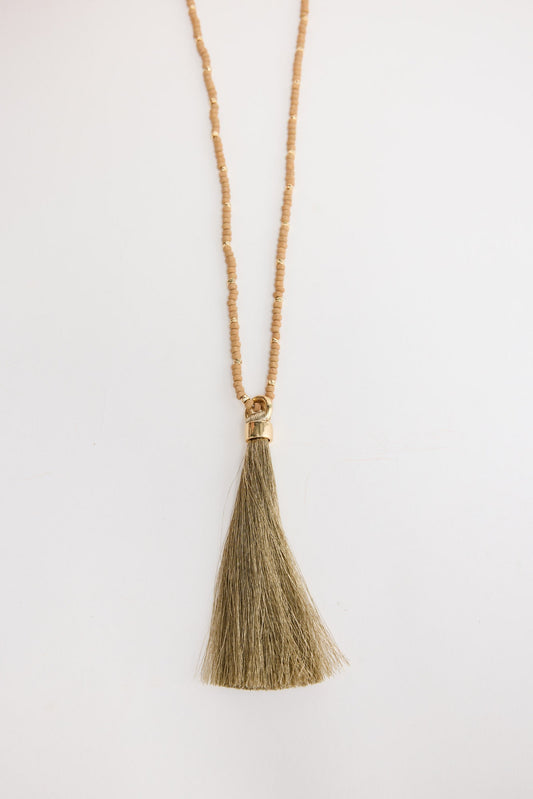 Close-up of the Mckenzie Necklace in taupe worn around the neck, showing the beaded strand and olive-tone tassel pendant