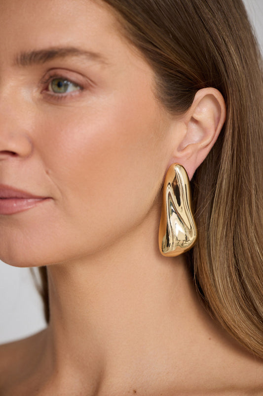 Close-up of a woman wearing a gold earring with a neutral background