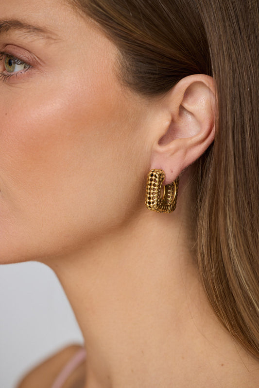 Model wearing Paloma Earrings in gold with textured finish, model close-up view on neutral background