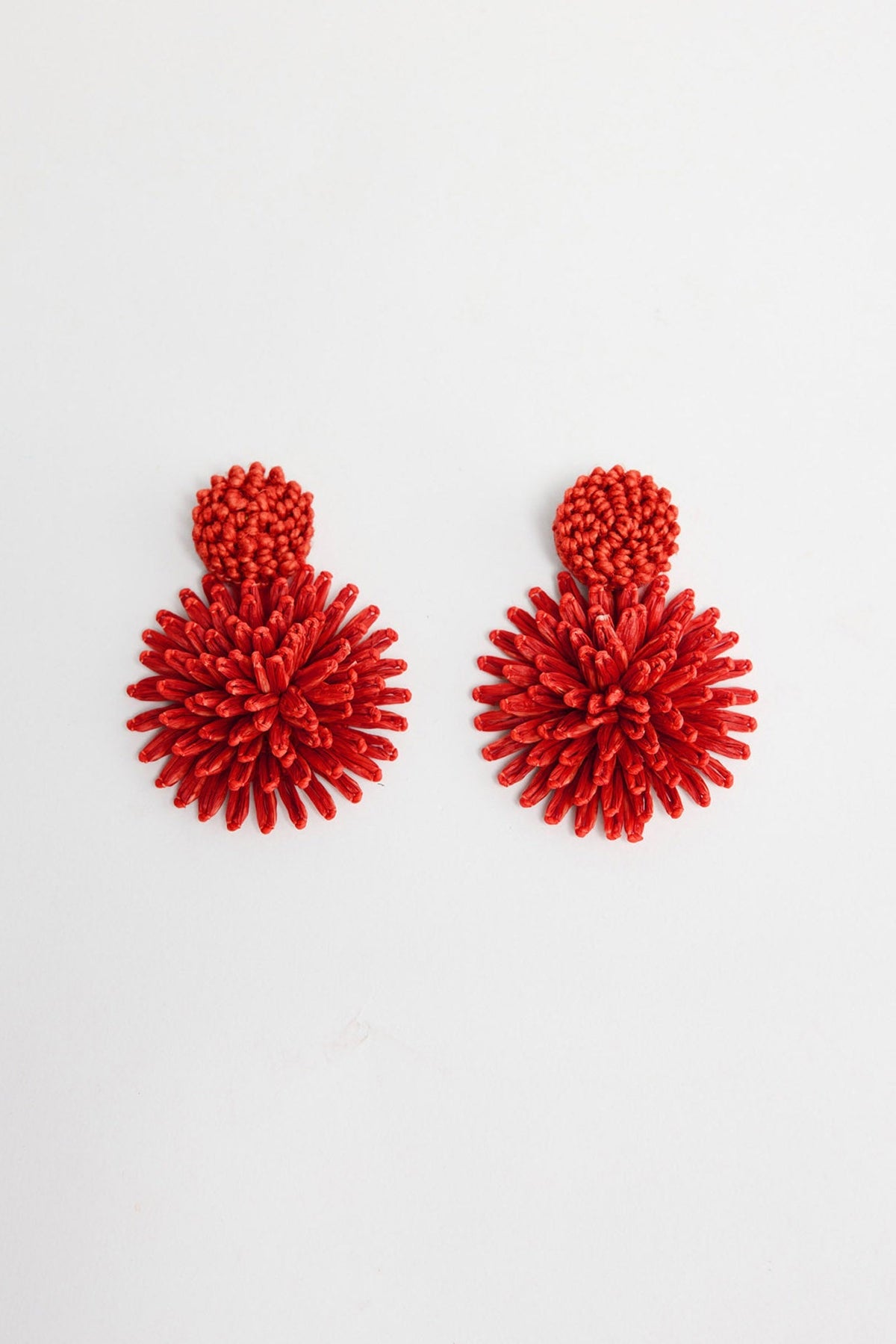 Pair of Polly statement earrings in Red showing the woven raffia burst design and round textured stud