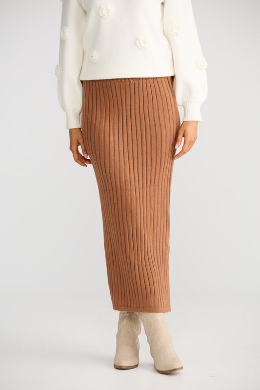 Person wearing a white top and brown ribbed skirt on a light gray background