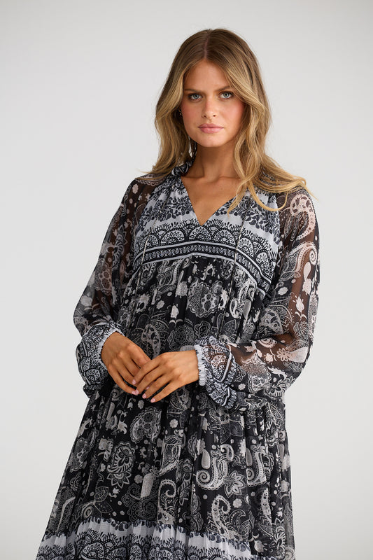 Woman wearing a long, patterned dress on a plain background