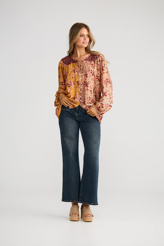 Woman wearing a patterned blouse and jeans on a white background