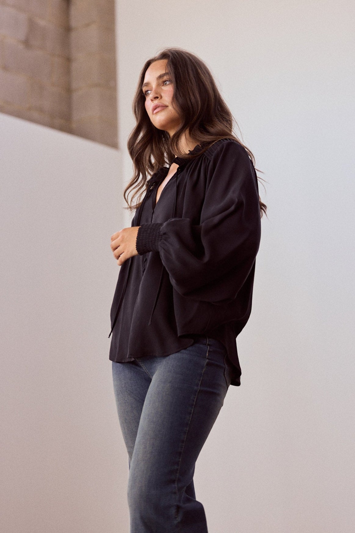 Model wearing Twilla Top in black with round neckline and mini ruffle trim, alternate view on white background