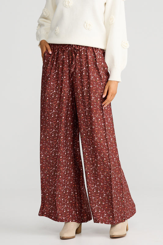 Person wearing maroon floral pants with a white top on a light gray background