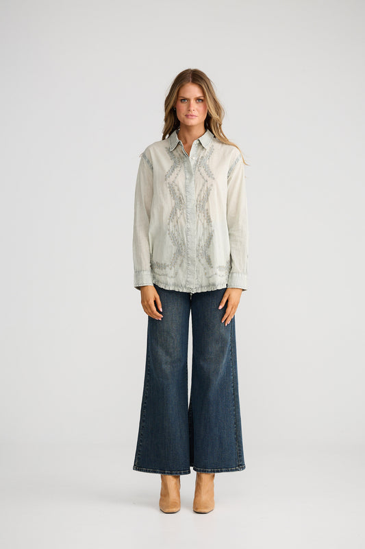 Woman wearing a light-colored shirt and dark jeans on a white background