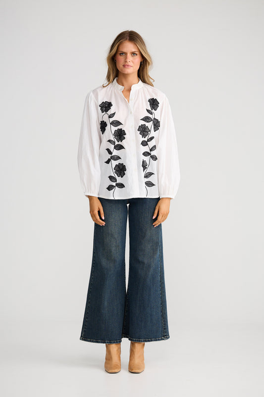 Woman wearing a white blouse with black floral patterns and blue jeans on a white background