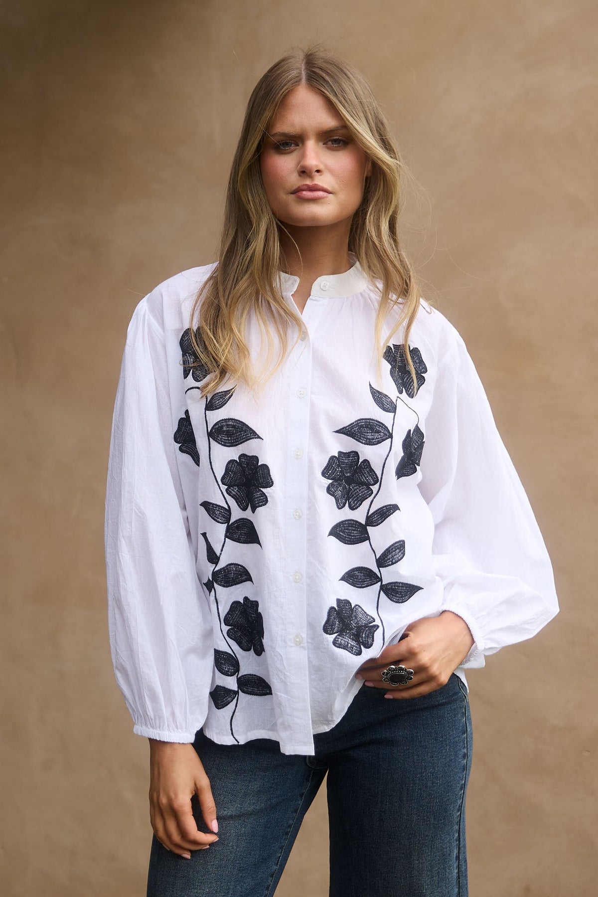 Woman wearing a white blouse with black floral embroidery against a beige background