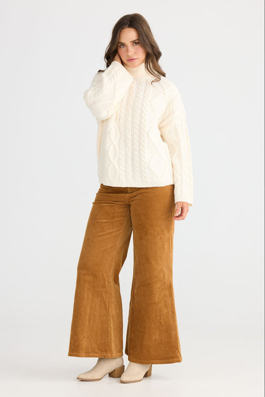 Model wearing Dixie Knit in cream with roll-neck collar and cable knit design, back view on white background