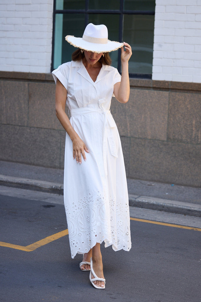 Woman in a white dress and hat walking on a street.