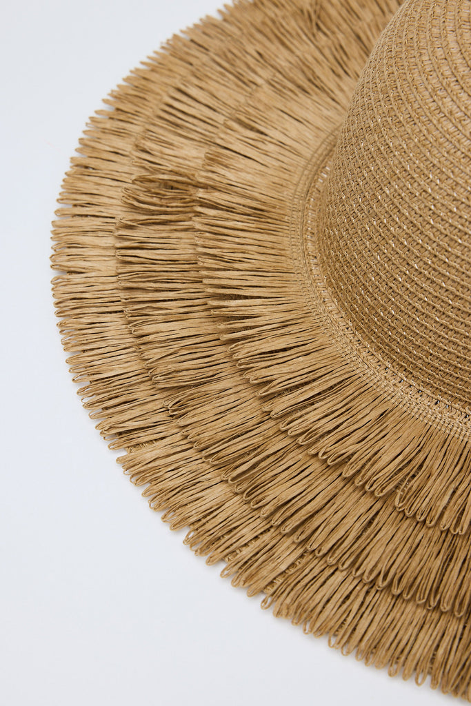 Close-up of a straw hat with fringe details on a light gray background