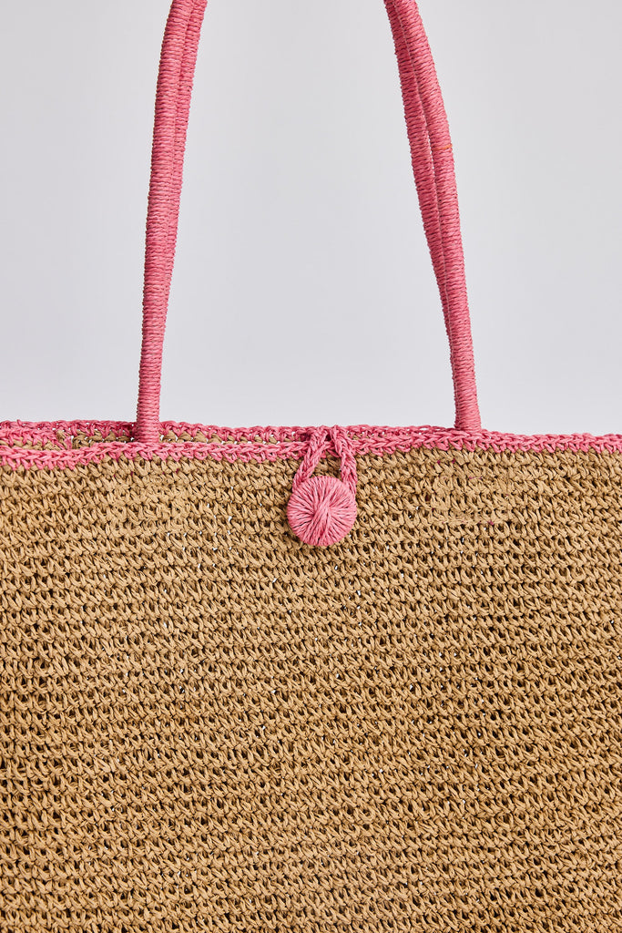 Close-up of a woven bag with pink handle and decorative element on a light gray background