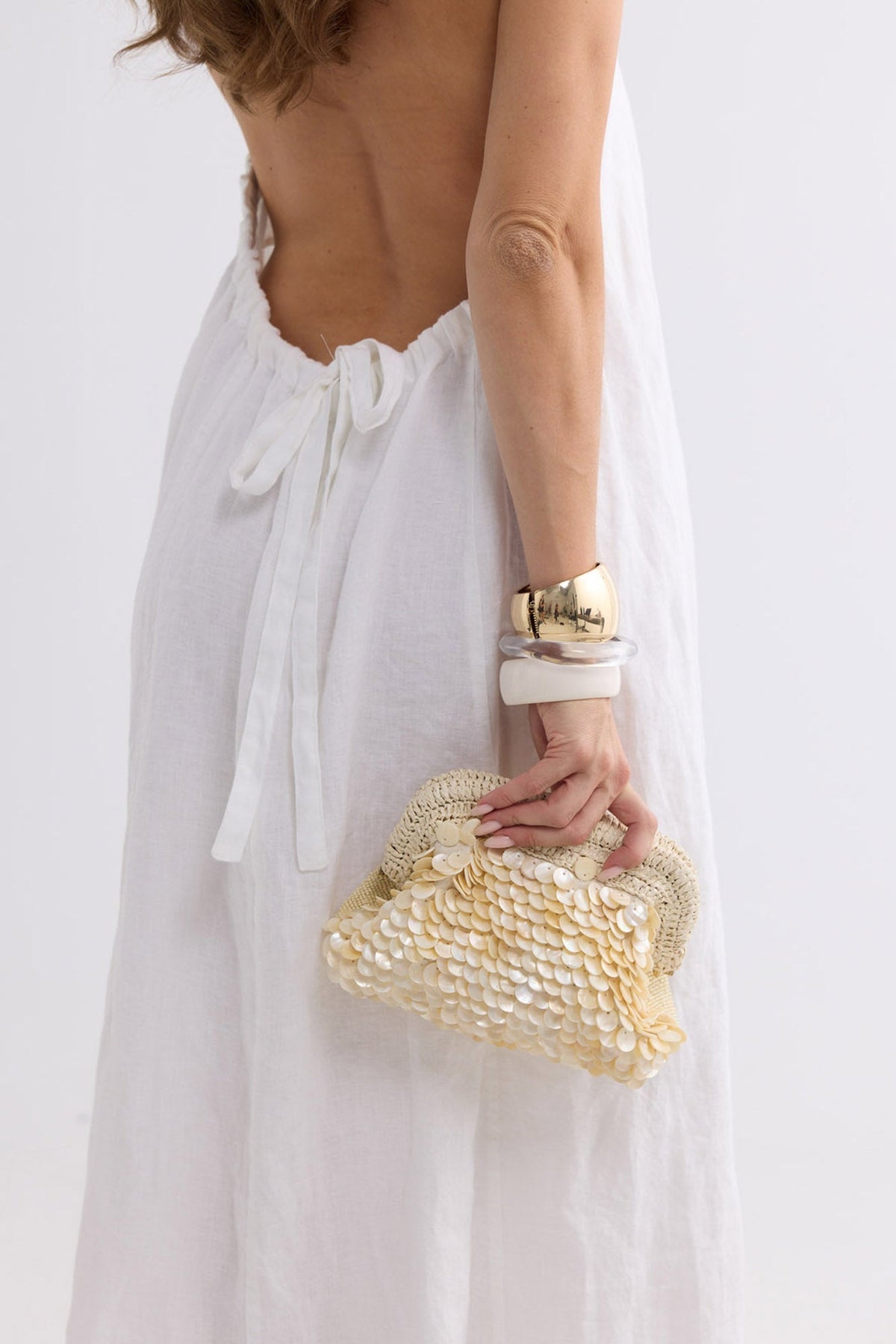 Sandy Clutch in creme held behind the back, worn with a backless white linen dress