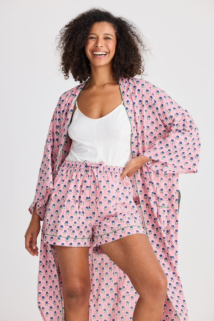 Woman wearing a pink floral kimono robe over a white top and shorts on a light gray background