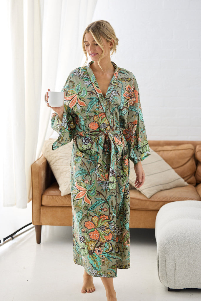 Woman wearing a floral robe holding a mug in a living room.