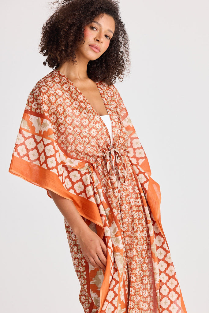 Woman wearing an orange and white patterned kimono-style garment on a white background