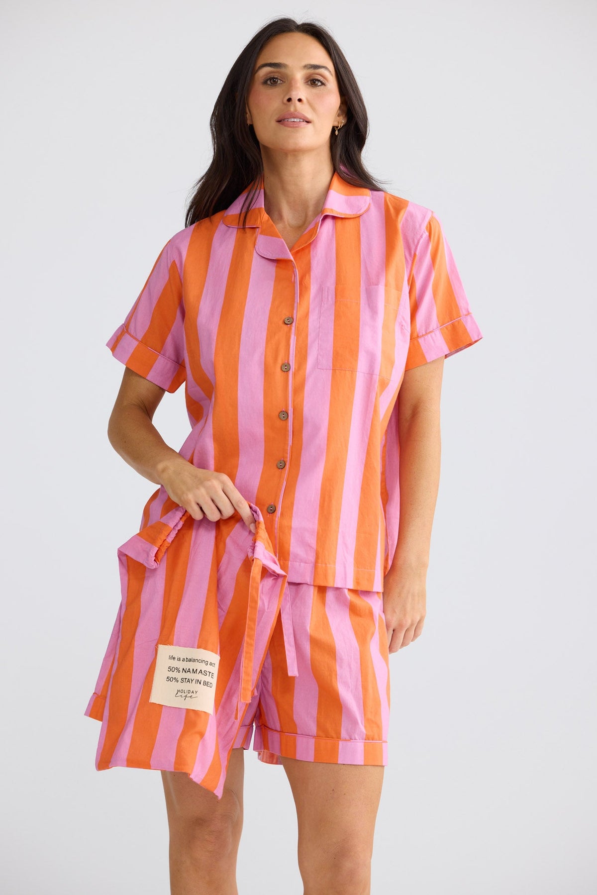 Model wearing Namaste Pyjama Set in lilac with orange stripe, front view, holding the matching drawstring bag.