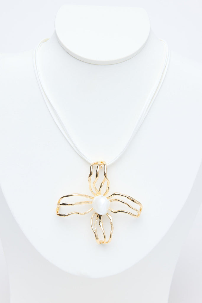 Gold flower pendant on a white necklace against a white background