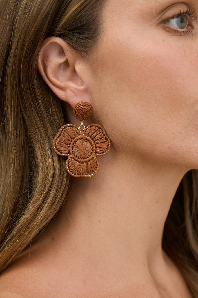Close-up of a woman wearing brown floral earrings with a neutral background