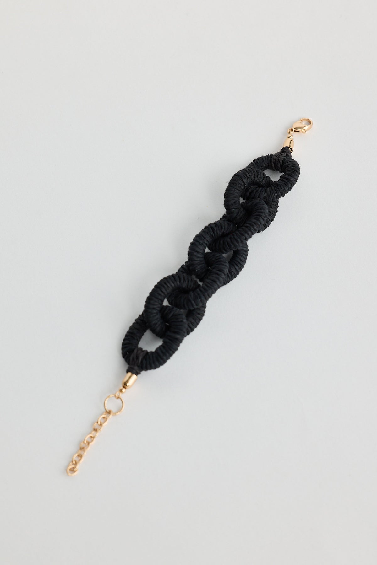 Black braided hair tie with gold clasp on a light gray background