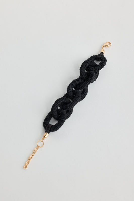 Black braided hair tie with gold clasp on a light gray background