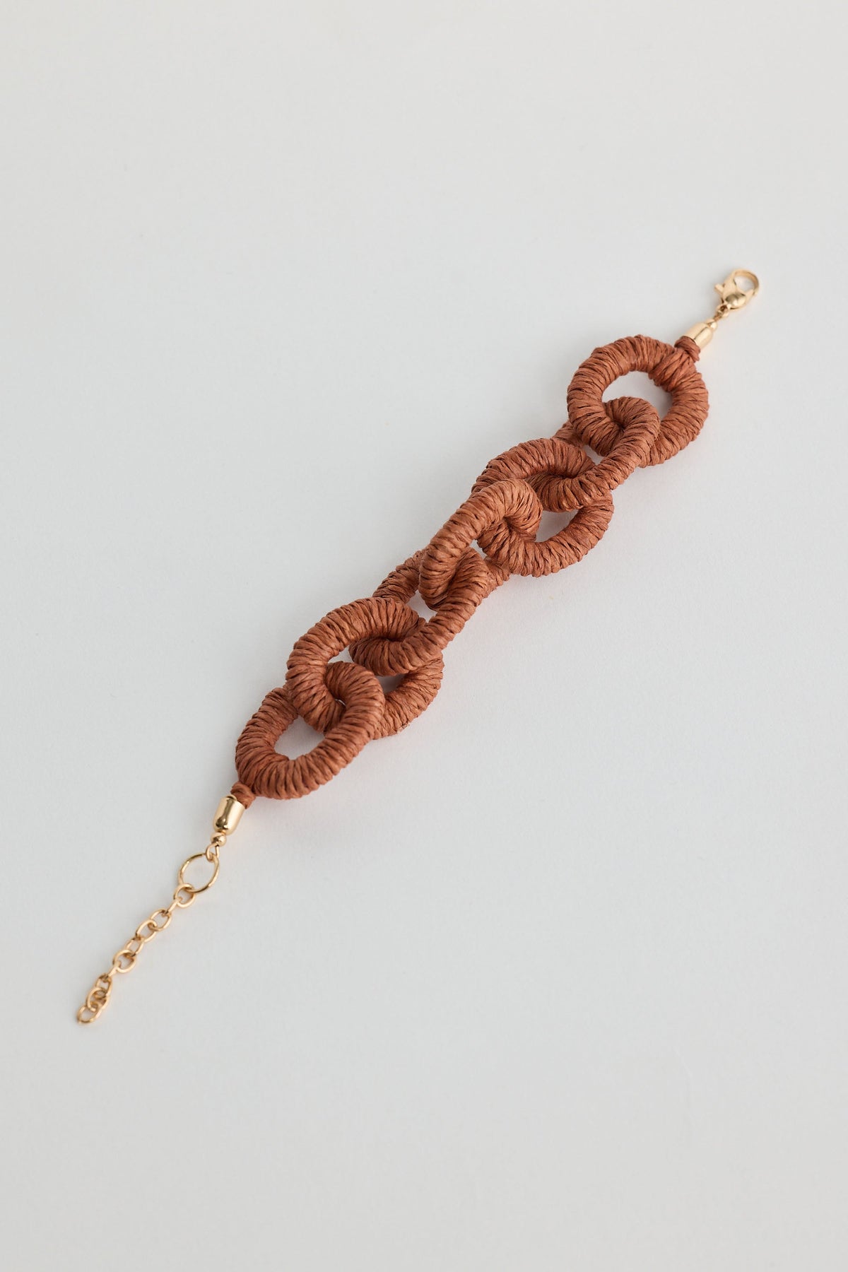 Brown braided bracelet with gold clasp on a light gray background