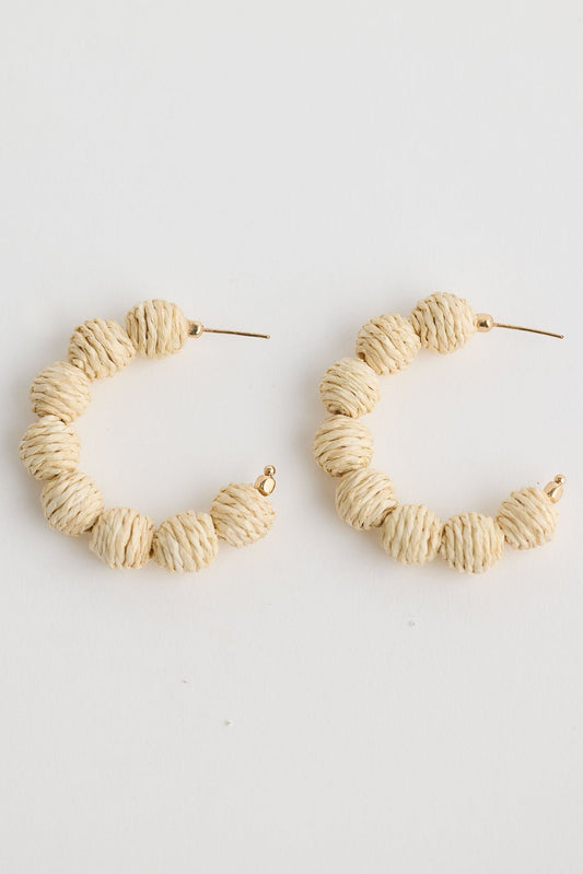 Pair of beige hoop earrings on a light gray background