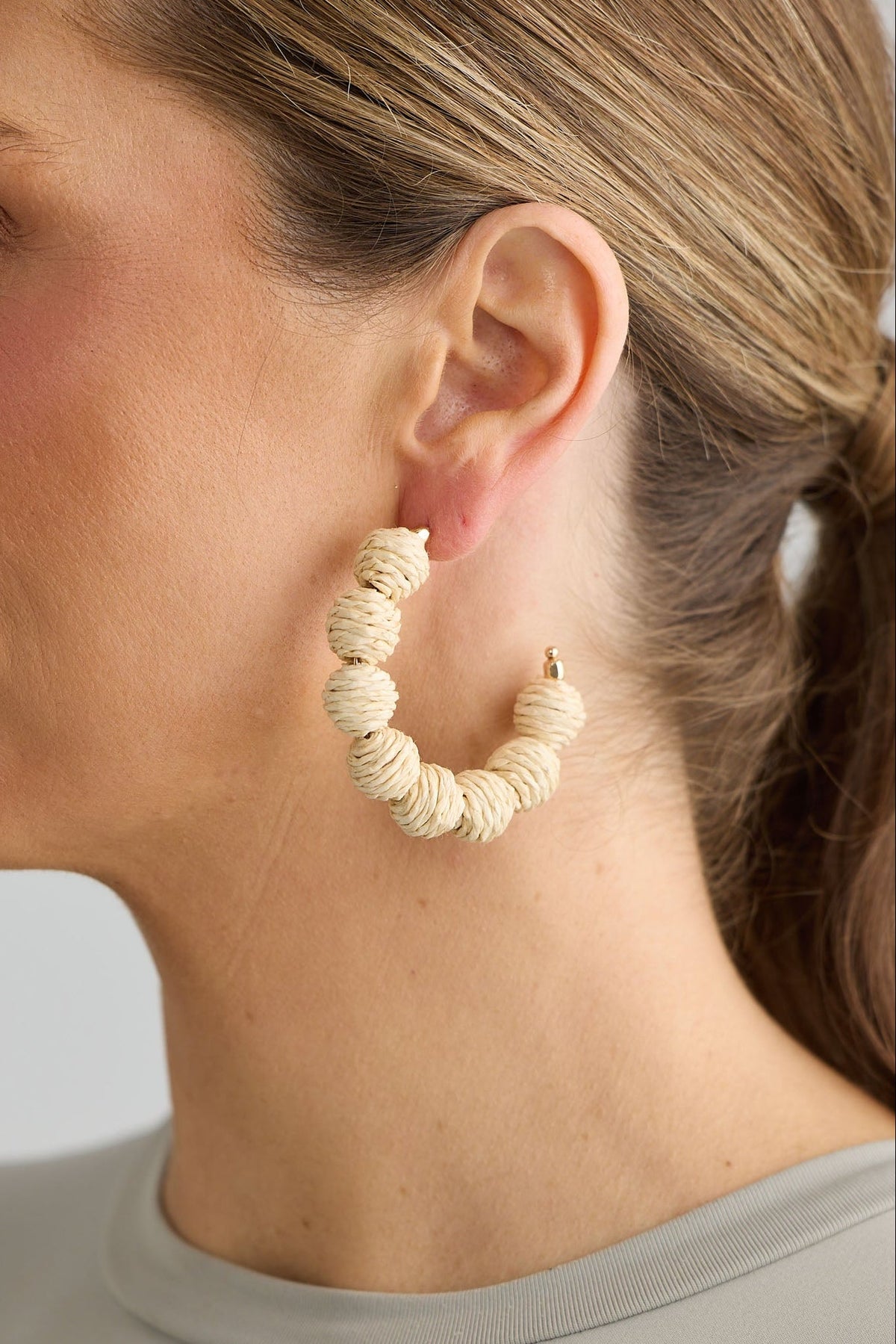 Woman wearing beige hoop earrings against a neutral background