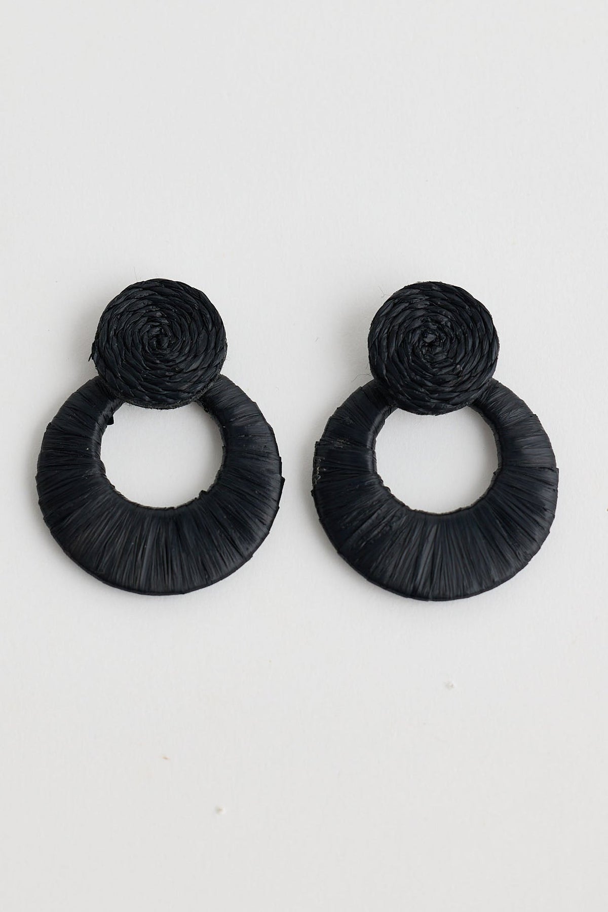 Pair of black raffia earrings on a light gray background