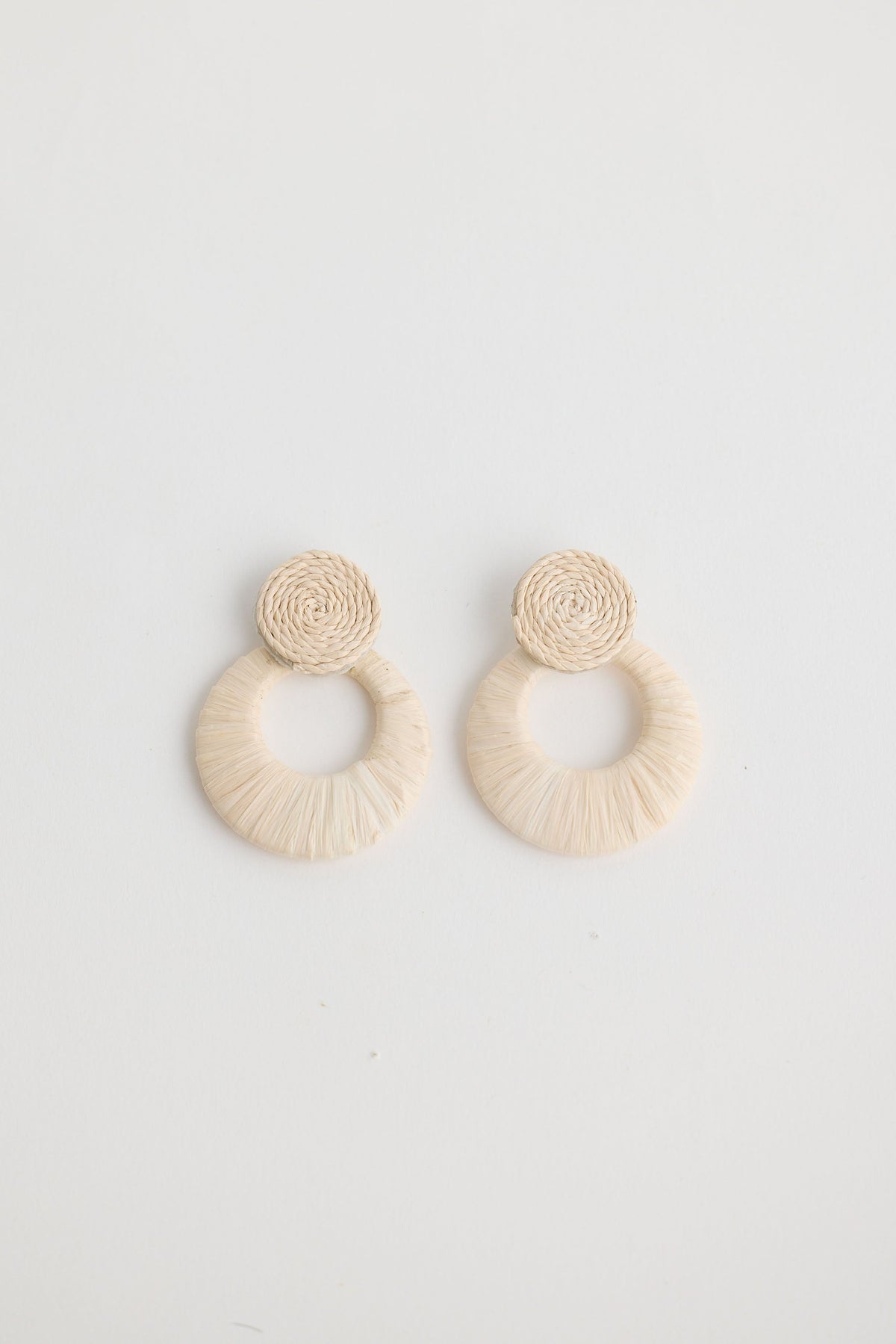 Pair of beige raffia hoop earrings on a light gray background