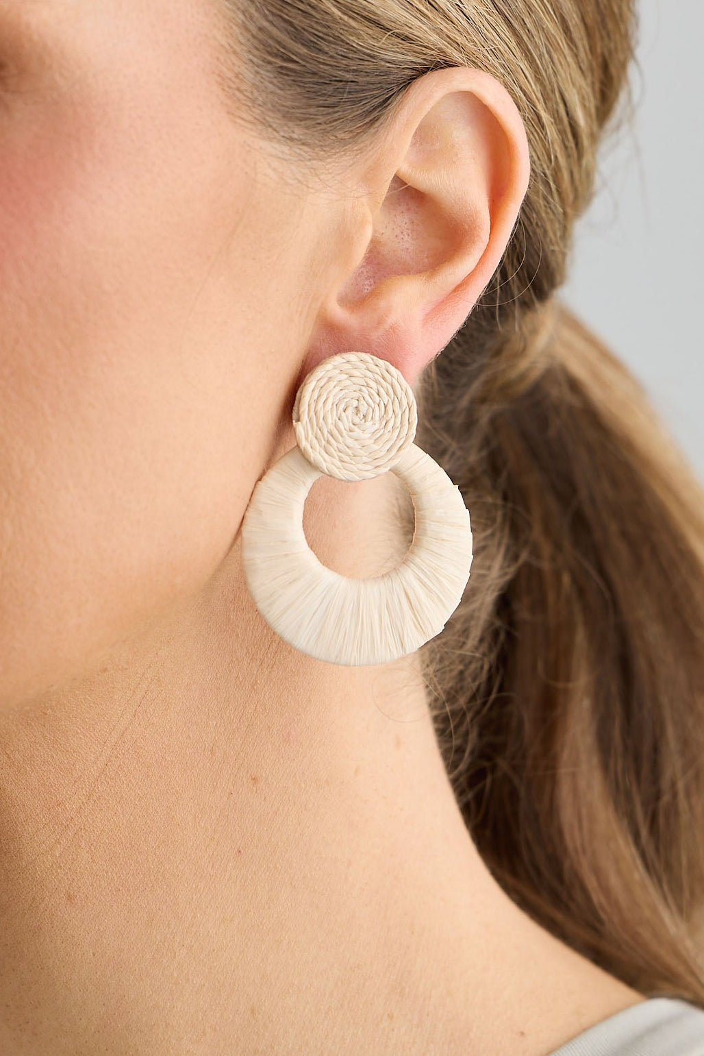 Woman wearing a pair of large, round earrings with a neutral background