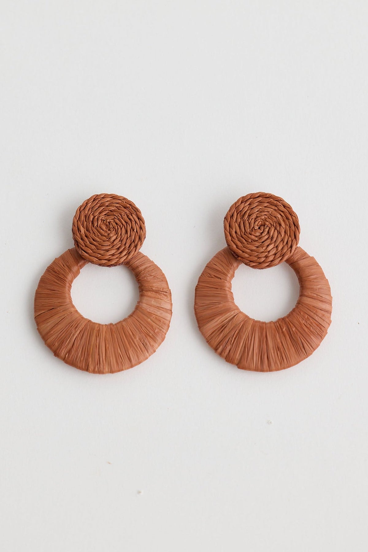 Pair of brown raffia earrings on a light gray background