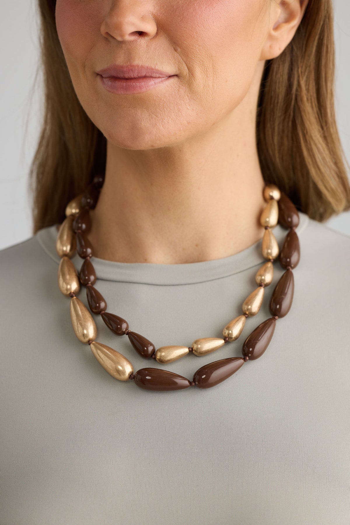 Woman wearing a brown and gold necklace against a neutral background