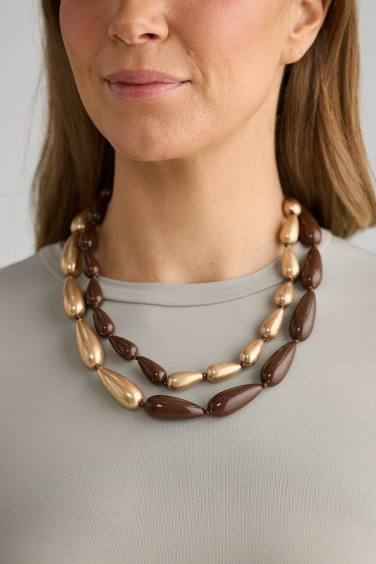 Woman wearing a brown and gold necklace against a neutral background