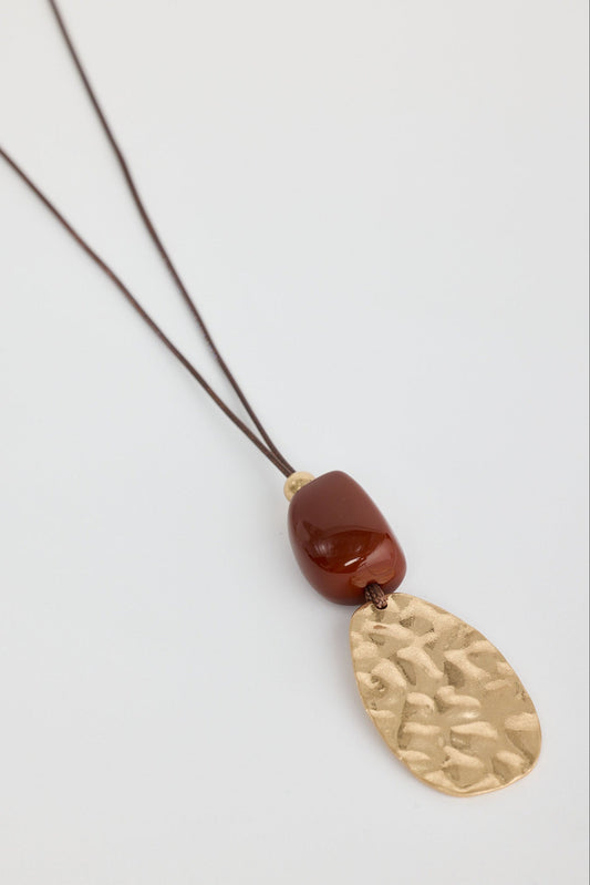 Necklace with a gold pendant and red bead on a light gray background