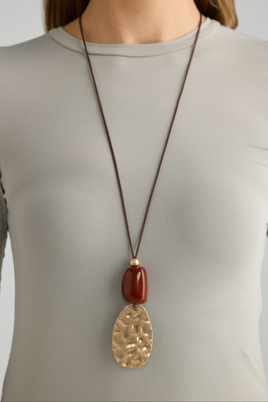 Long necklace with a large pendant worn by a person in a plain shirt