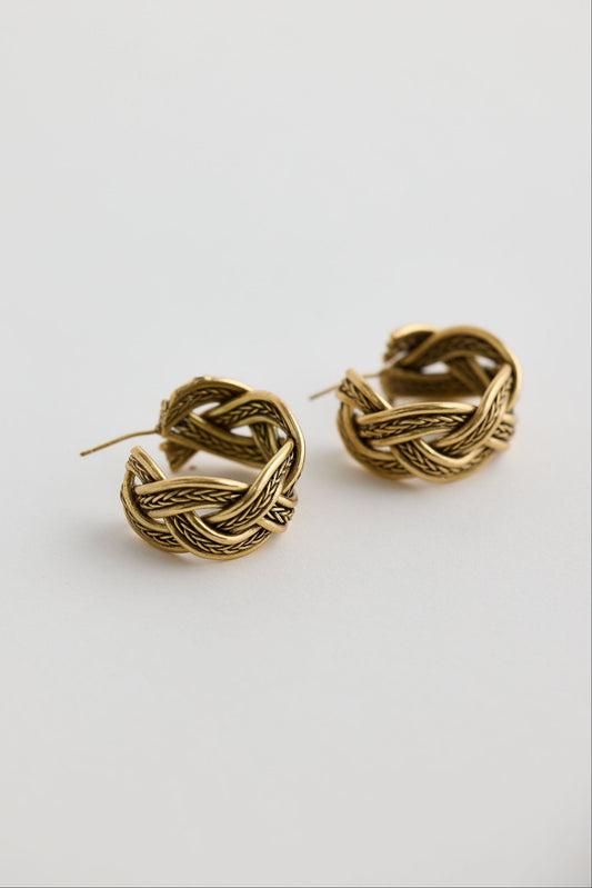 Pair of gold braided hoop earrings on a light gray background