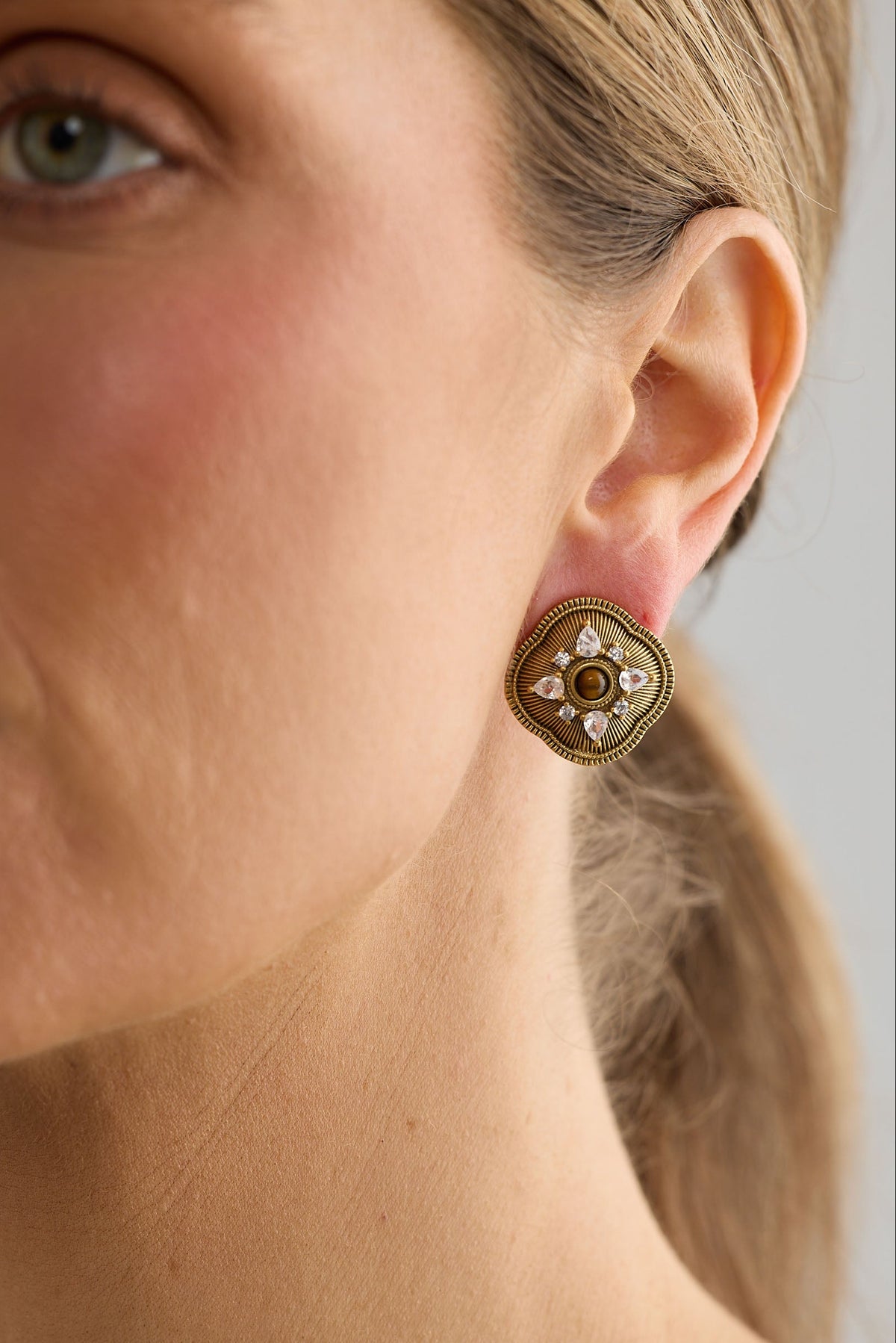 Close-up of a woman wearing a gold earring with a floral design.