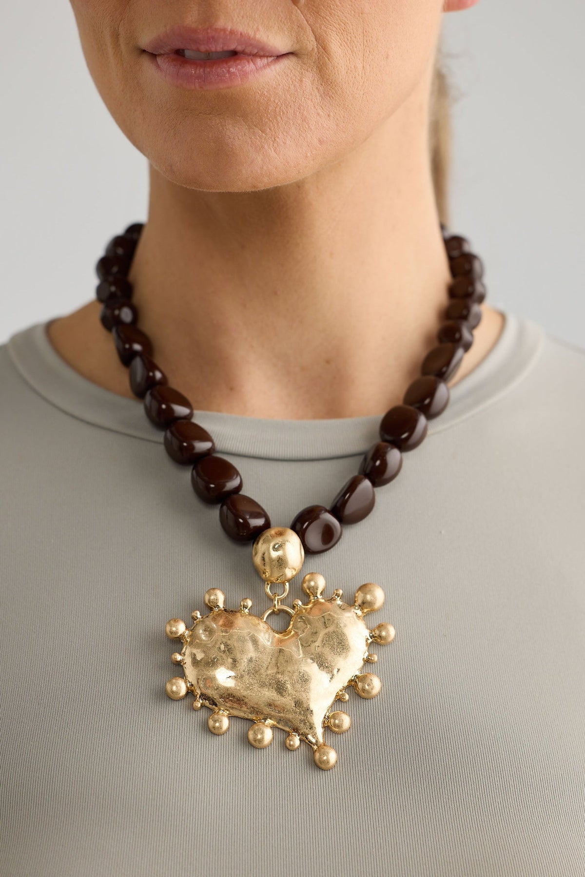 Necklace with a large gold heart pendant worn by a person on a plain background