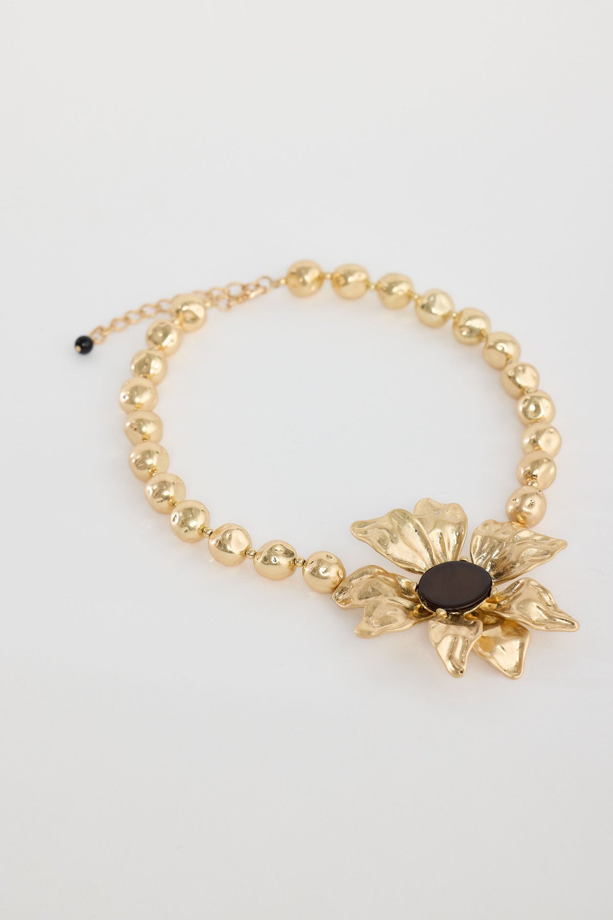 Gold bracelet with a floral design and dark bead on a light gray background