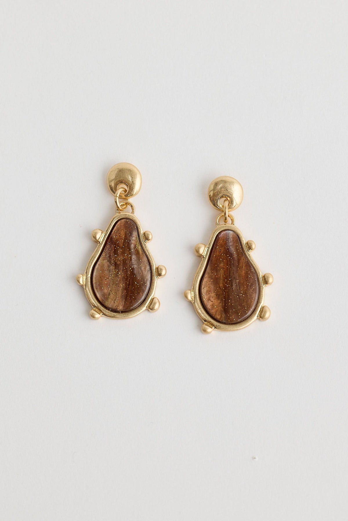 Pair of gold earrings with brown teardrop-shaped stones on a light gray background