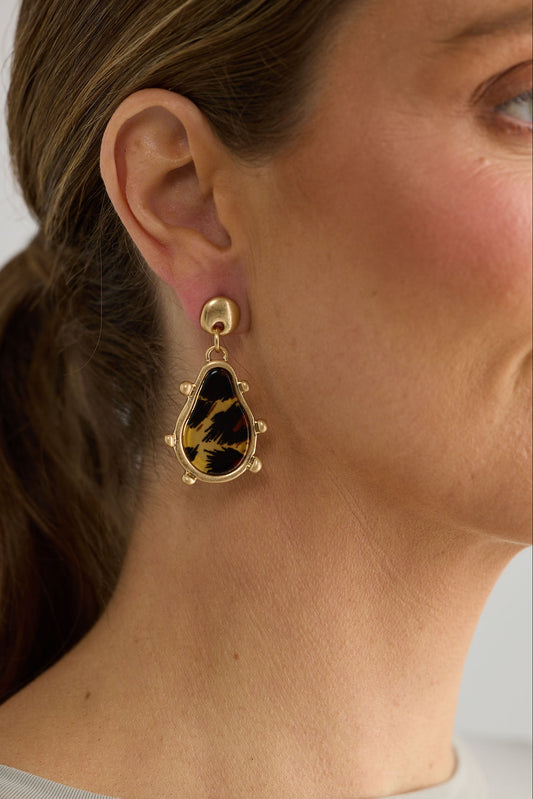 Close-up of a person wearing a gold and black earring with a neutral background