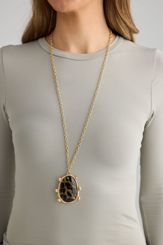 Person wearing a gold necklace with a leopard print pendant on a plain background