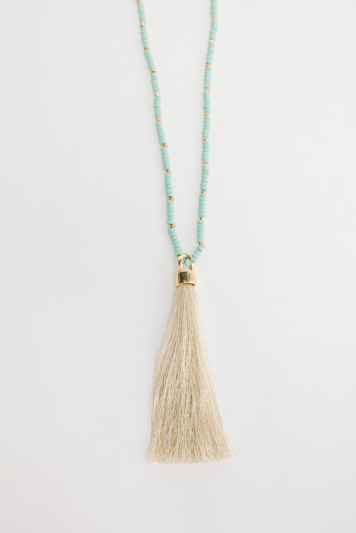 Long aqua-blue seed bead necklace with gold-tone spacer beads and a large cream silk tassel pendant with a gold cap, shown flat on a white background