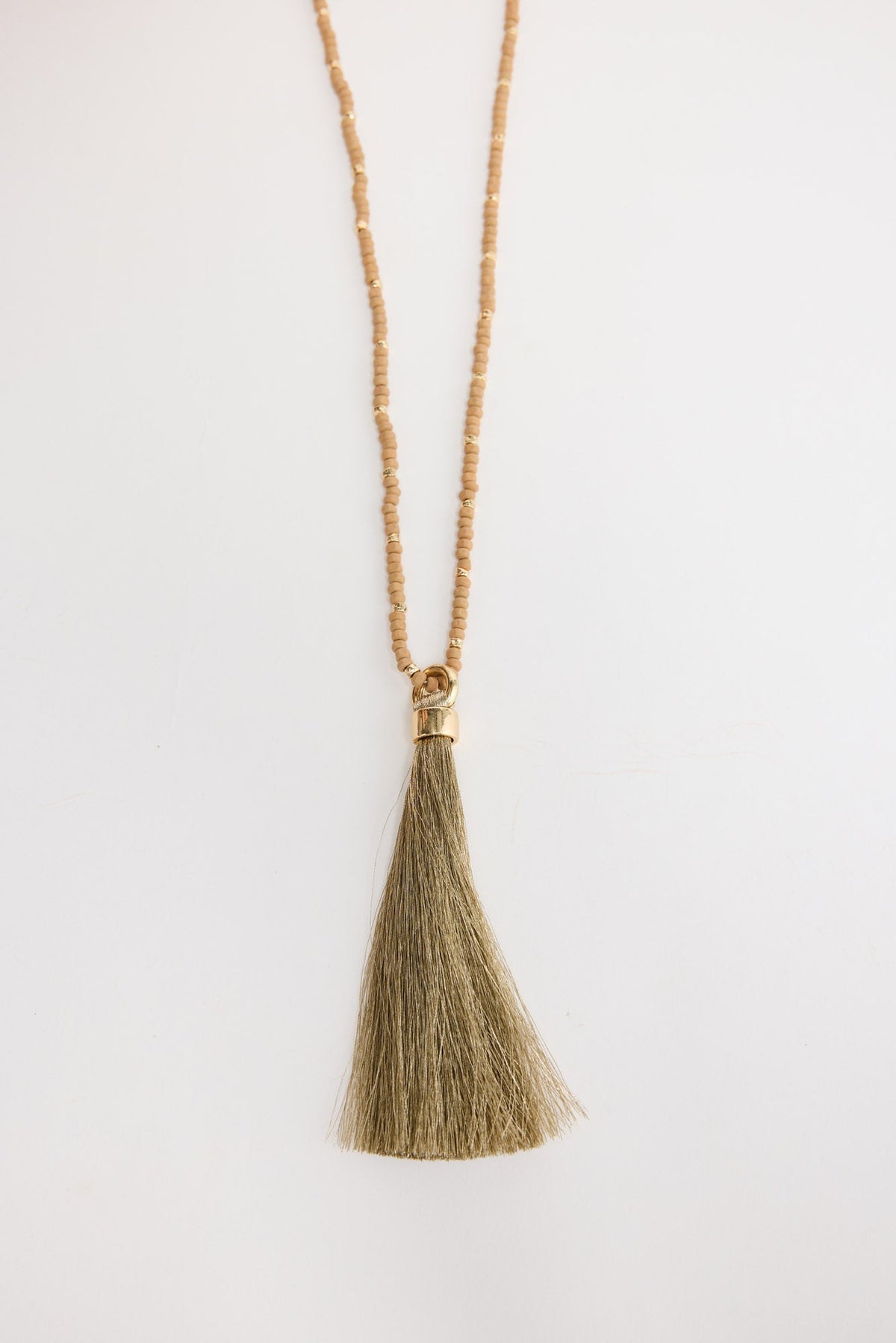 Close-up of the Mckenzie Necklace in taupe worn around the neck, showing the beaded strand and olive-tone tassel pendant