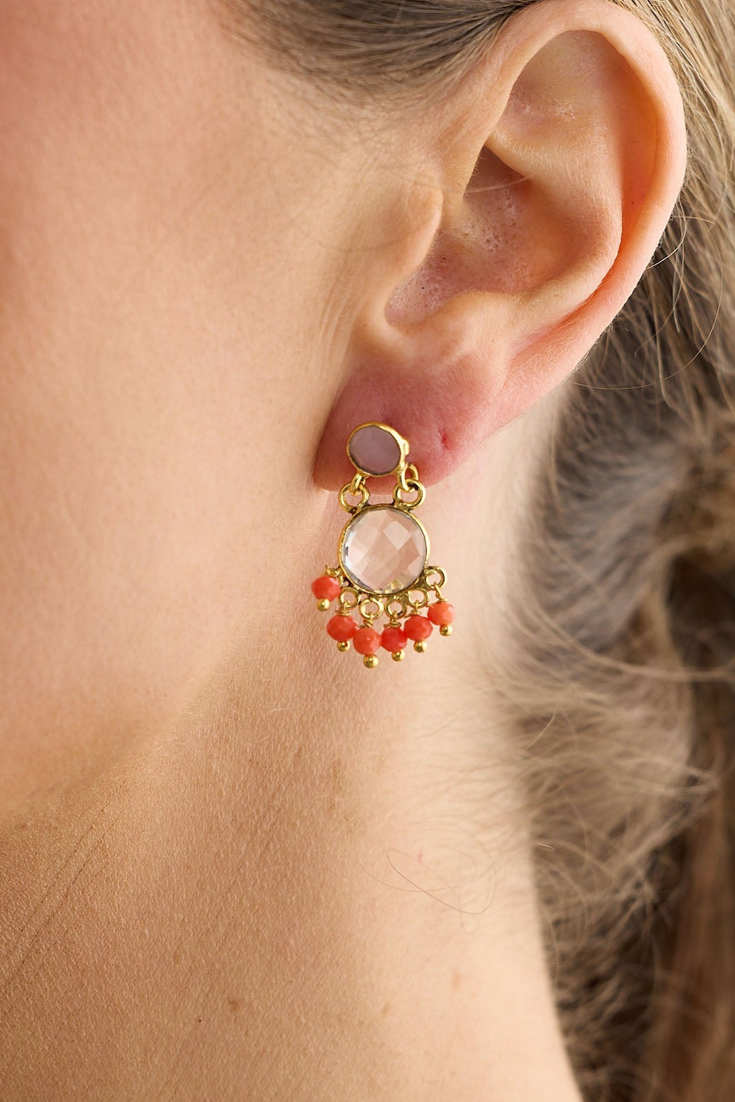 Close-up of a woman wearing a gold earring with red stones against a neutral background