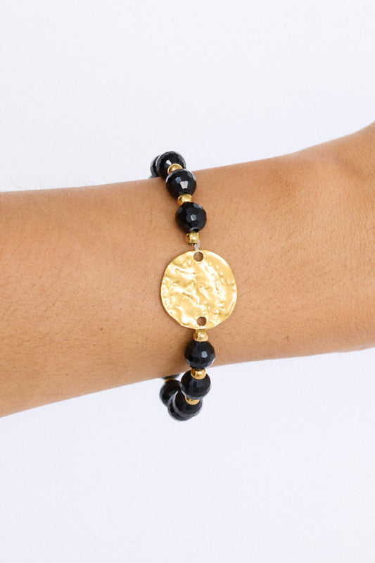 Model wearing Taylor Bracelet in black with statement gold charm detail, angled on-wrist view on neutral background
