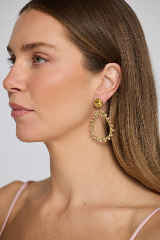 Model wearing Sawyer Earrings in blush with delicate beaded trim detailing, model close-up view on neutral background