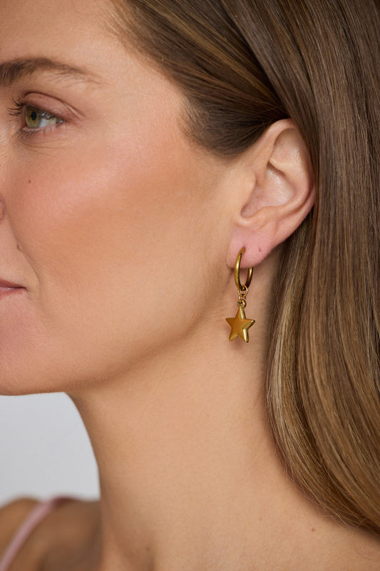 Model wearing Star Gaze Earrings in gold with bold star charm detail, model close-up view on neutral background